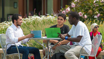 Three students talking around a table on American University's campus